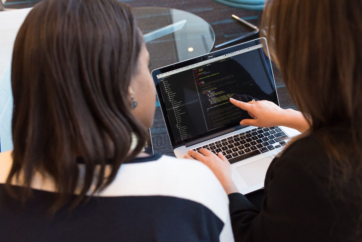 Two people reviewing syntax-highlighted code on a silver MacBook