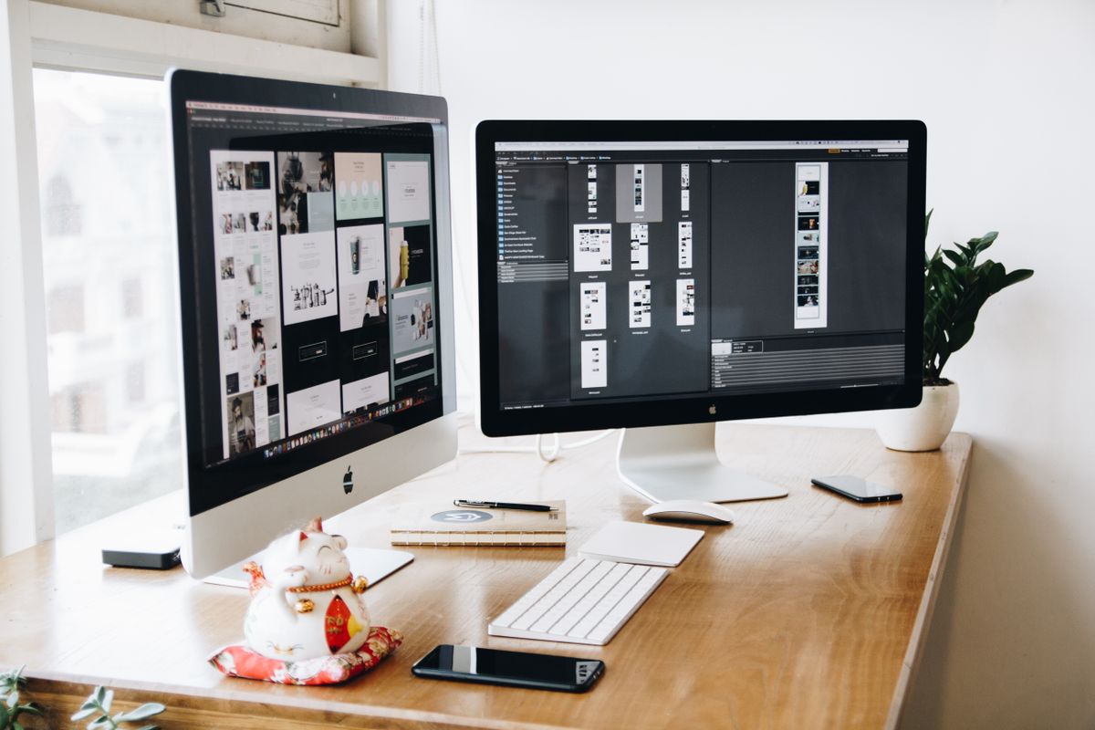 two Apple iMacs, iPhone, keyboard on a wooden desk